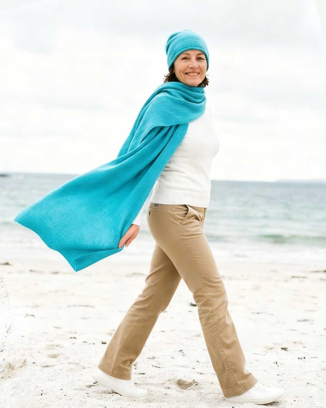 Woman walking on an irish beach wearing a turquoise cashmere scarf.