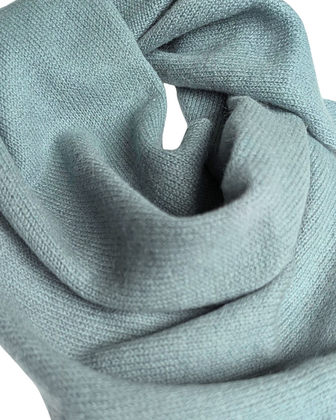 A close-up of a soft knit neck scarf in a muted sage green colour, draped to show its fine ribbed texture against a white background.