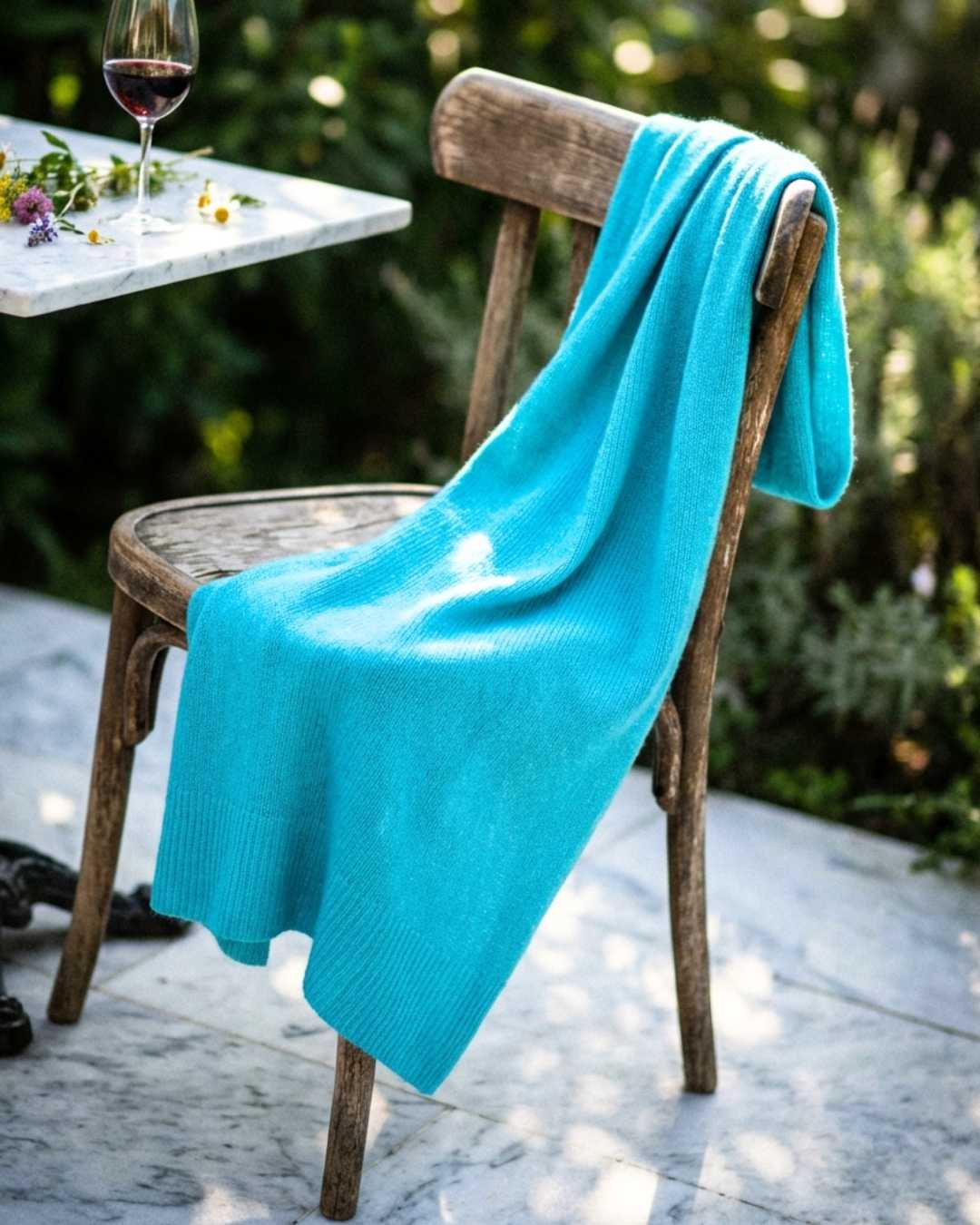 Turquoise blanket draped over a wooden chair outdoors with a blurred background