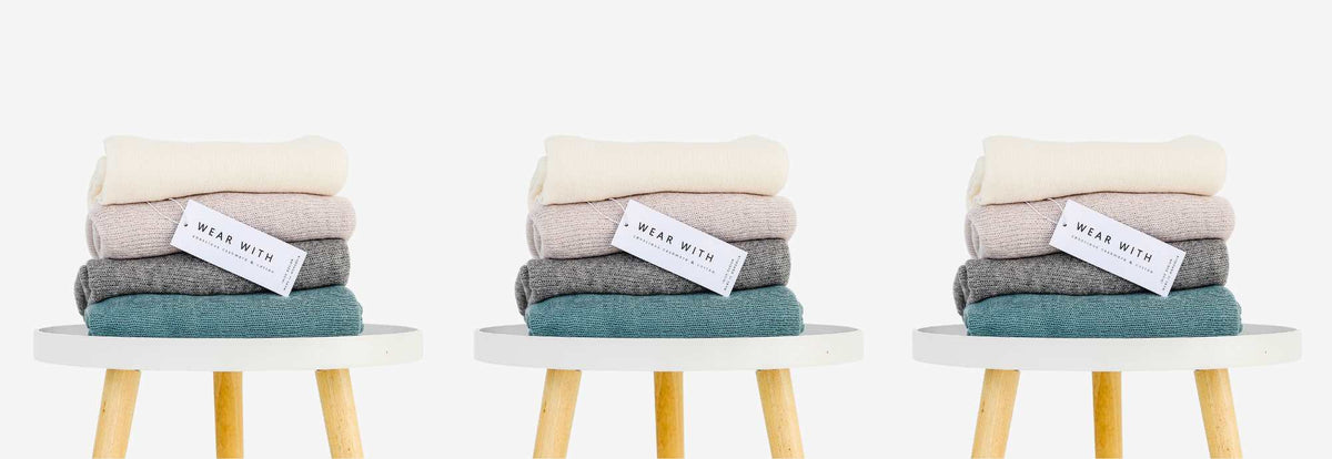 Stack of luxury women's cashmere scarves in soft cream, pink, grey, and teal designed in Ireland