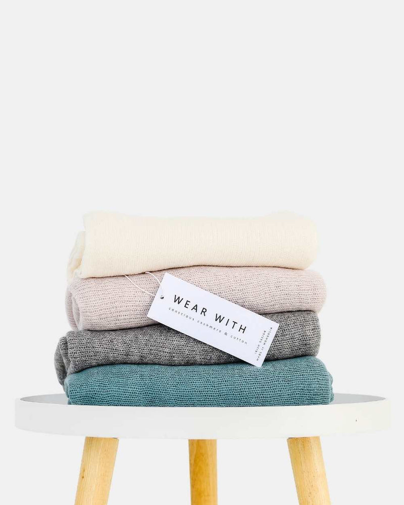 Stack of luxury women's cashmere scarves in soft cream, pink, grey, and teal designed in Ireland